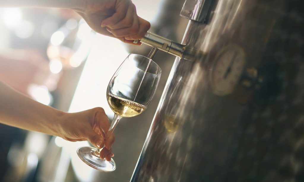 Pouring white wine out of stainless steel wine tank.