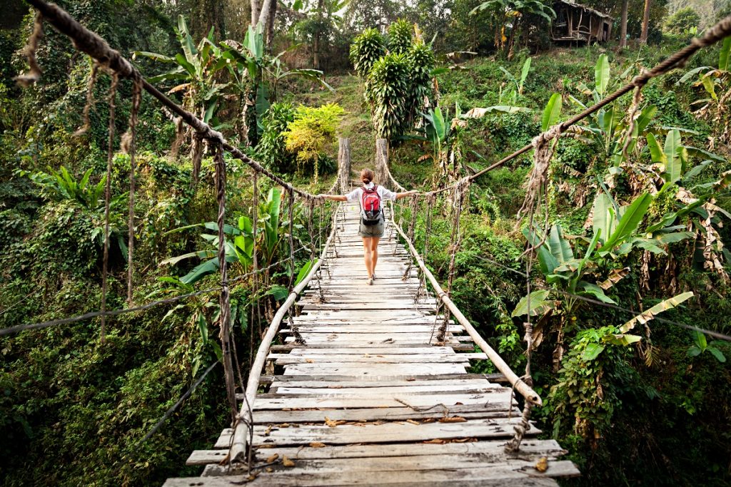 Single woman with backpack on suspension bridge in rainforest
